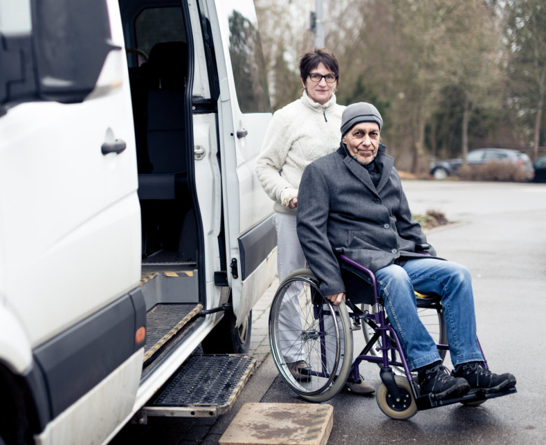 woman assisting elderly man in wheelchair beside the car