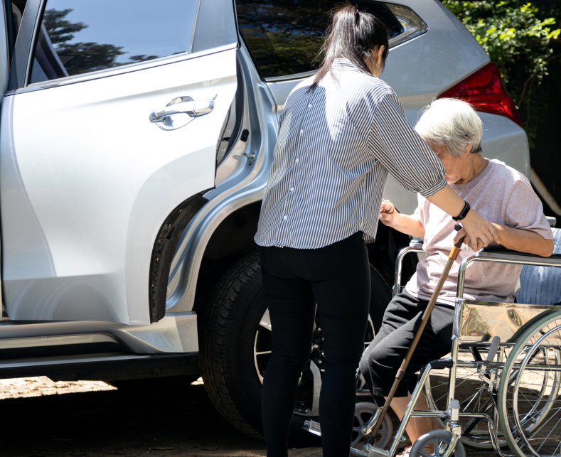 woman assisting elderly man in wheelchair beside the car