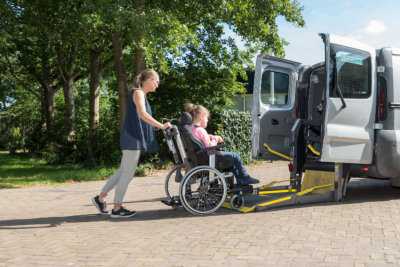 a child on wheelchair and her carer boarding into a van